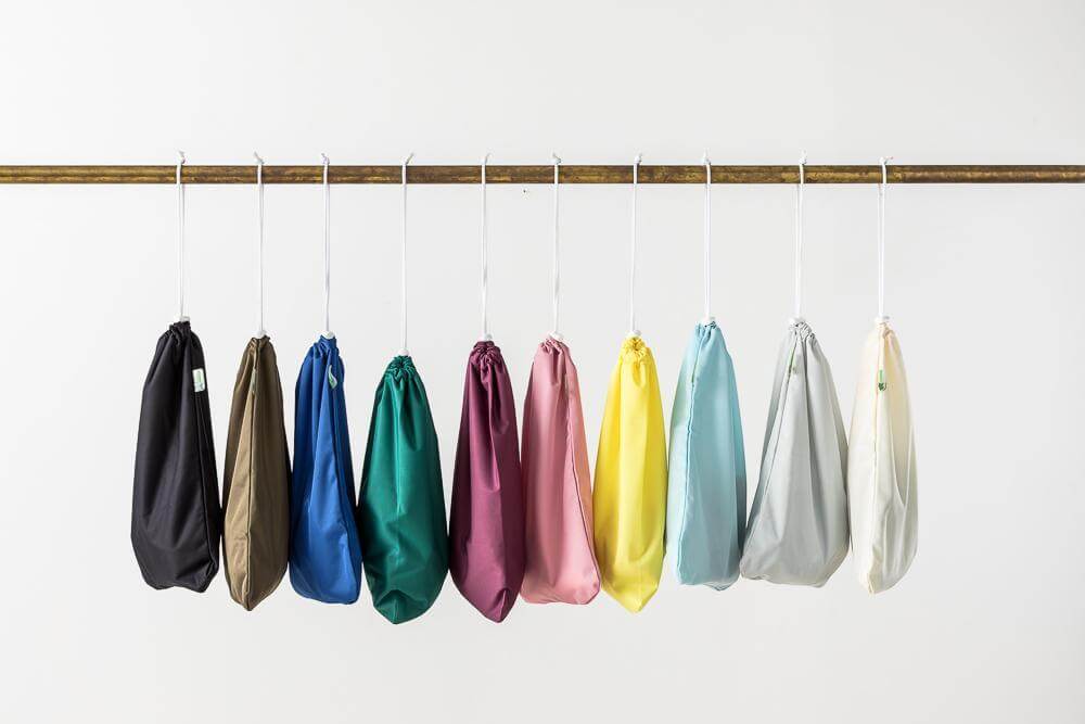 Collection of colorful Reusable Wet Nappy Bags and Baby Changing Essentials hanging on a rod.